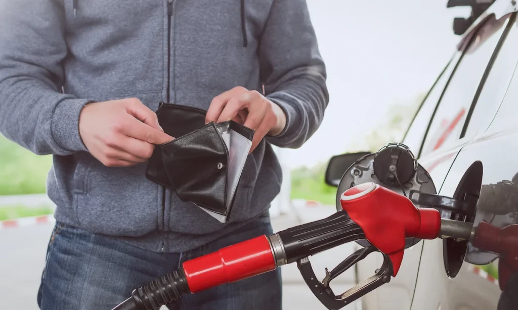 Lack of money for gasoline and fuel. Expensive gasoline. Driver man holds one dollar end empty wallet against the background of a fuel nozzle in the gas tank. increase in gasoline prices concept.