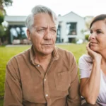 Woman with hand in head looking at man with white hair at backyard