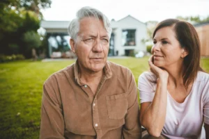 Woman with hand in head looking at man with white hair at backyard