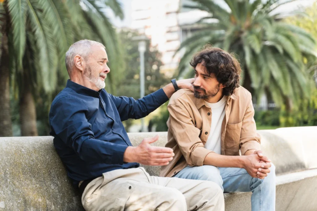 Two men sitting on a bench, having a conversation and offering support outdoors. Senior man giving advice