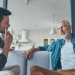 Handsome young man talking to his senior father while spending time at home together