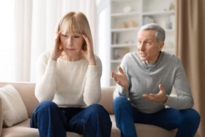 Stressed senior woman sitting on sofa during argument with husband at home