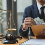 Young Asian lawyer or legal consultant holding money out of brown envelope with hammer and goddess of injustice on table The concept of corruption and embezzlement.