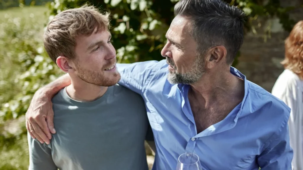 Mature man with wine glass embracing young man in garden