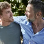 Mature man with wine glass embracing young man in garden