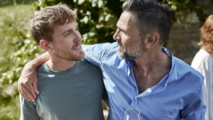 Mature man with wine glass embracing young man in garden