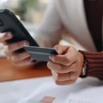 Business person, hands and phone with credit card for online transaction, purchase or banking at office. Employee, document or user with mobile smartphone or debit for ecommerce app or remote payment