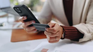 Business person, hands and phone with credit card for online transaction, purchase or banking at office. Employee, document or user with mobile smartphone or debit for ecommerce app or remote payment