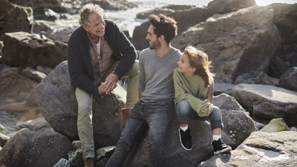 Happy grandfather, father and son sitting on rock at the coast