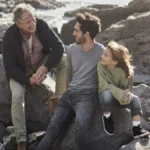 Happy grandfather, father and son sitting on rock at the coast