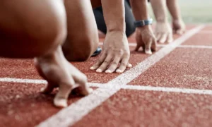 Ground, hands and people ready for a race, running competition or training at a stadium. Fitness, sports and athlete runners in a line to start a sprint, exercise or challenge in track or athletics